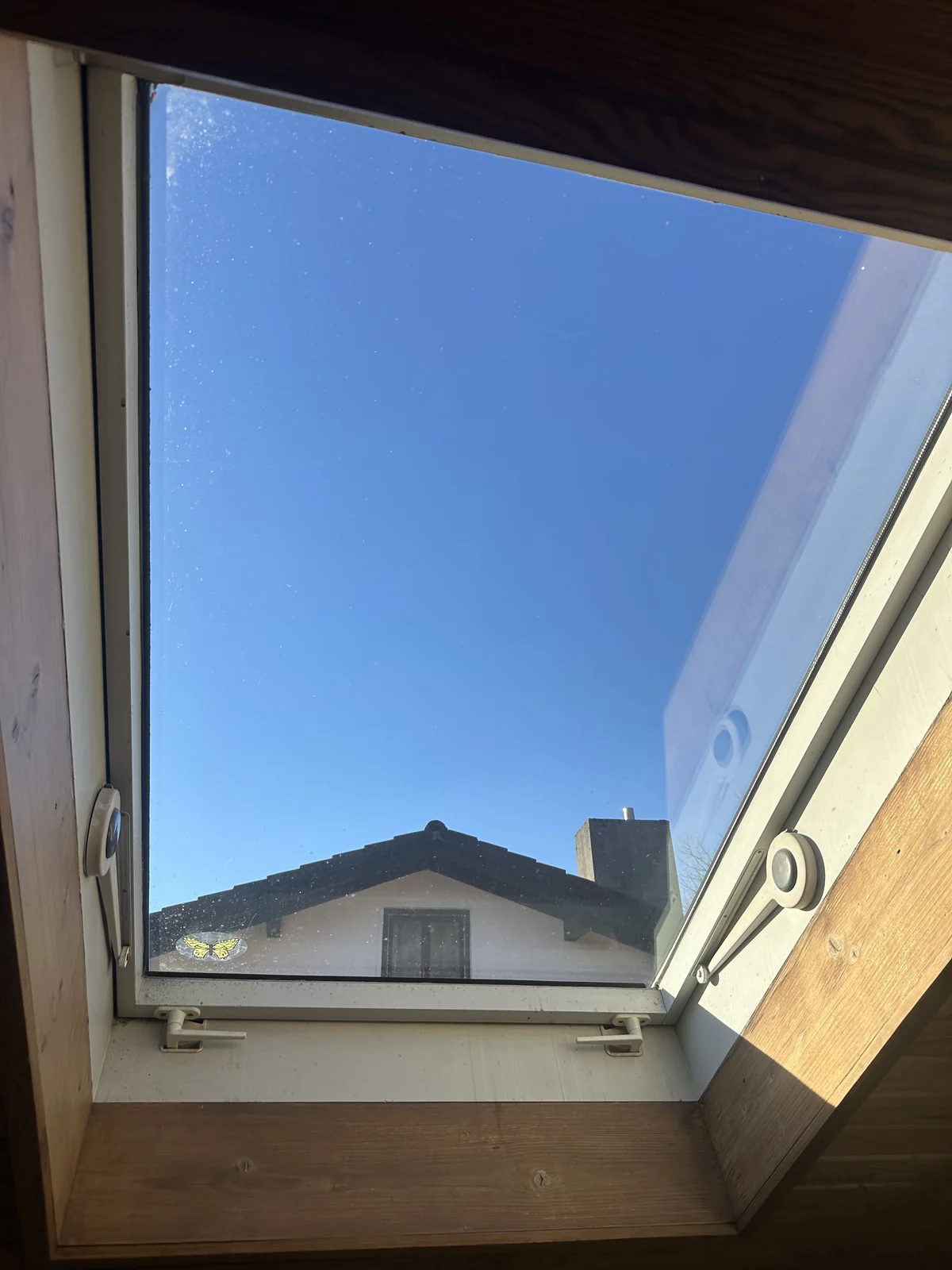 Geöffnetes Dachfenster mit Holzrahmen vor blauem Himmel