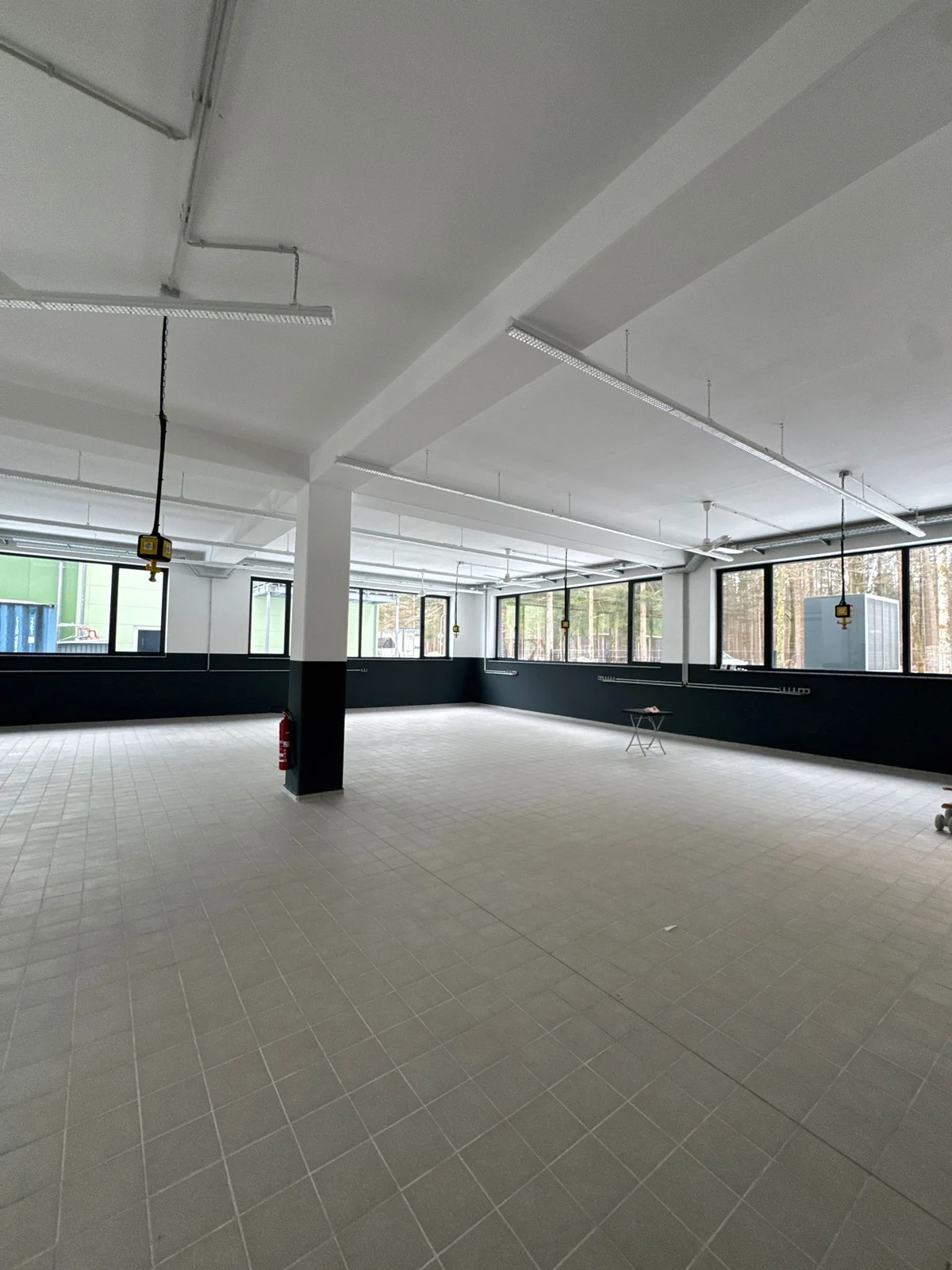 Leerer Gewerberaum mit großen Fenstern, Deckenleuchten und sichtbaren Leitungen