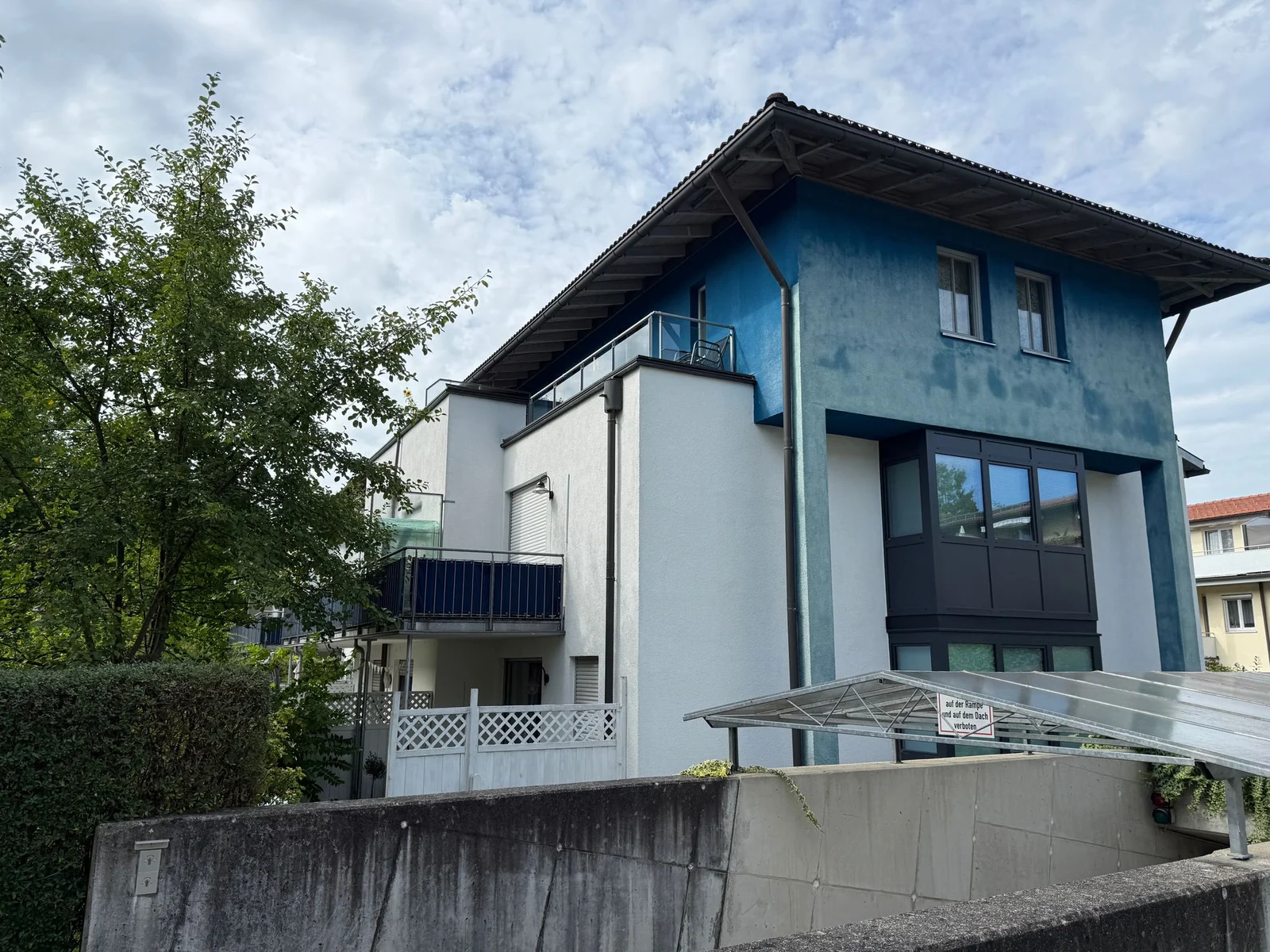 Mehrgeschossiges Wohnhaus mit blauer Putzfassade, Balkonen und verglastem Vorbau