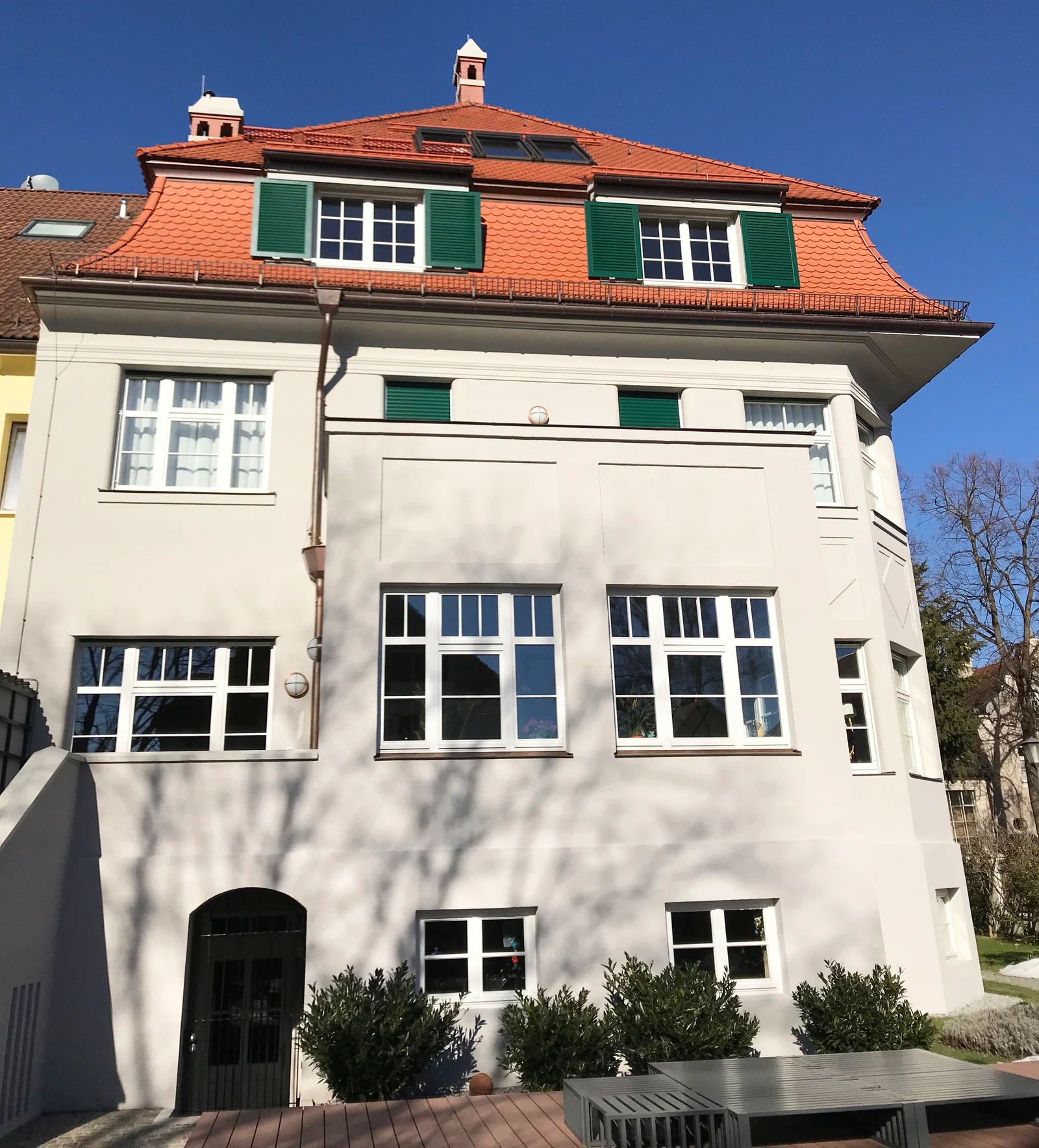 Älteres Wohnhaus mit gegliedertem Ziegeldach, grünen Fensterläden und heller Putzfassade