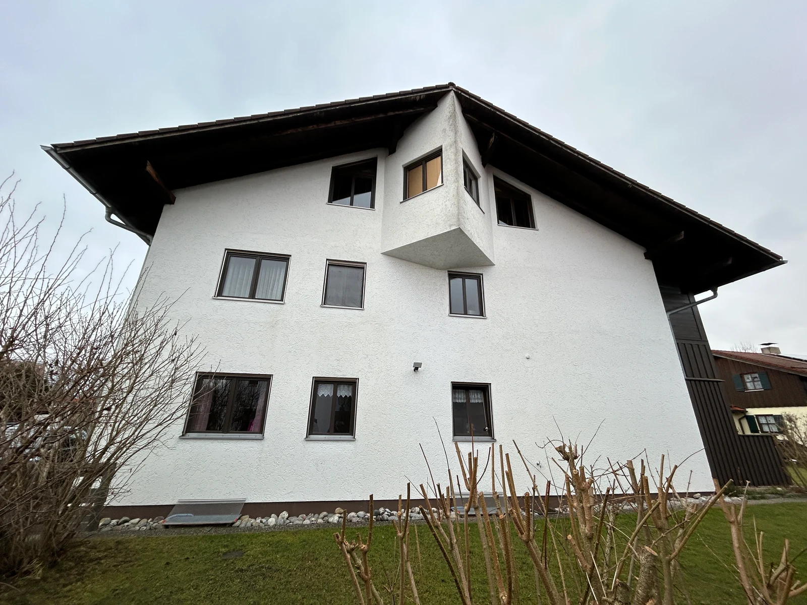 Wohnhaus mit breitem Dachüberstand, vorspringendem Erker und bestehenden dunklen Fensterrahmen